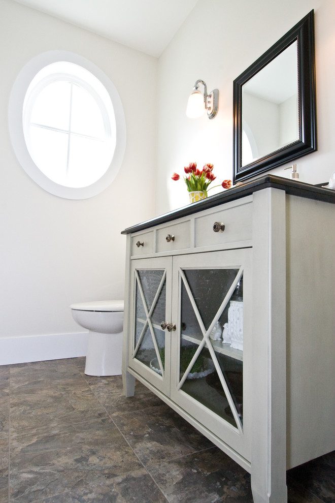 Mid-sized traditional powder room in Vancouver with glass-front cabinets, grey cabinets, white walls, brown floor and black benchtops.