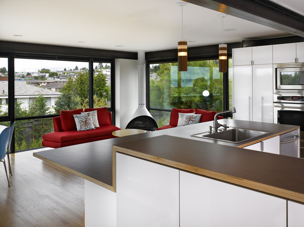 Photo of a modern open plan kitchen in Seattle with a drop-in sink, flat-panel cabinets, white cabinets, laminate benchtops and stainless steel appliances.