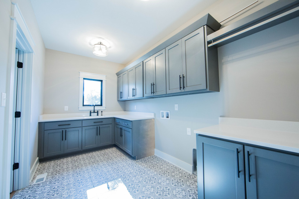 Inspiration for a large country single-wall dedicated laundry room in Indianapolis with an undermount sink, recessed-panel cabinets, grey cabinets, quartz benchtops, beige walls, porcelain floors, a side-by-side washer and dryer, grey floor and white benchtop.