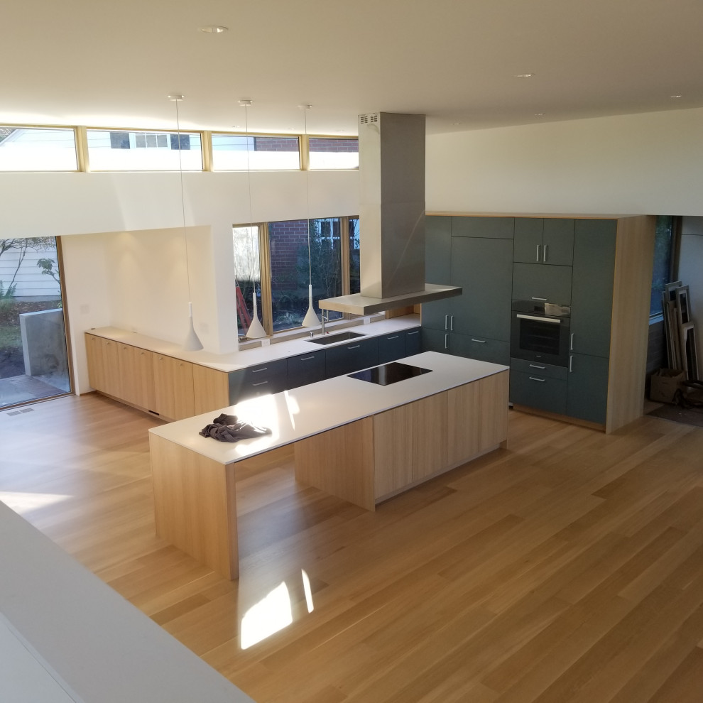 Medium sized modern open plan kitchen in Seattle with light hardwood flooring, a single-bowl sink, flat-panel cabinets, light wood cabinets, composite countertops, white splashback, black appliances, an island, beige floors, white worktops and a vaulted ceiling.