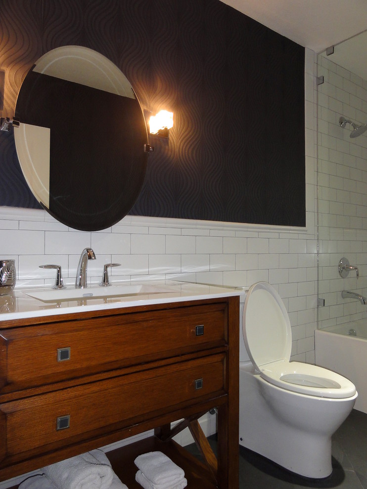Mid-sized transitional bathroom in Miami with an integrated sink, medium wood cabinets, solid surface benchtops, a drop-in tub, a shower/bathtub combo, a two-piece toilet, white tile, ceramic tile, black walls and slate floors.