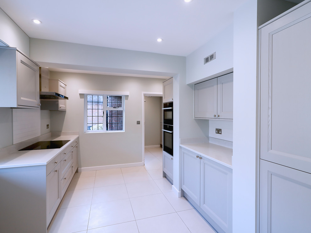 Cette image montre une cuisine minimaliste avec un placard à porte shaker, des portes de placard grises, un plan de travail en quartz et un plan de travail blanc.