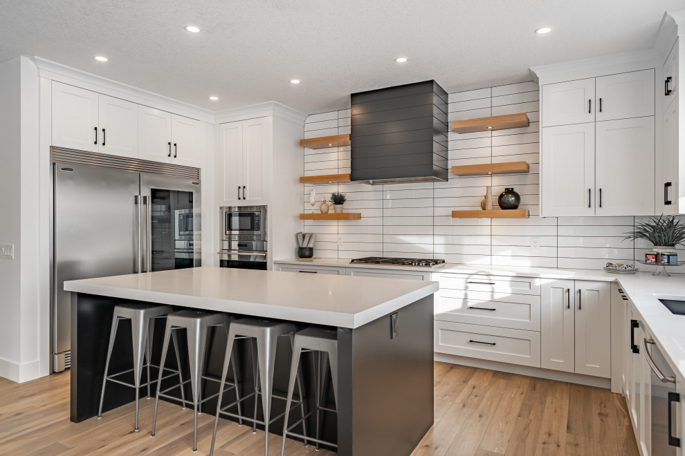 Kitchen - transitional u-shaped light wood floor kitchen idea in Calgary with shaker cabinets, white cabinets, white backsplash, stainless steel appliances, an island and white countertops