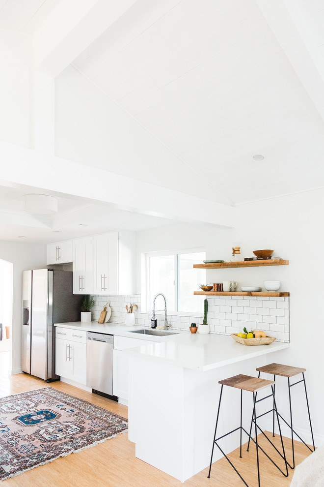 This is an example of a scandinavian kitchen in San Diego with a single-bowl sink, shaker cabinets, white cabinets, quartzite benchtops, white splashback, subway tile splashback, stainless steel appliances and bamboo floors.
