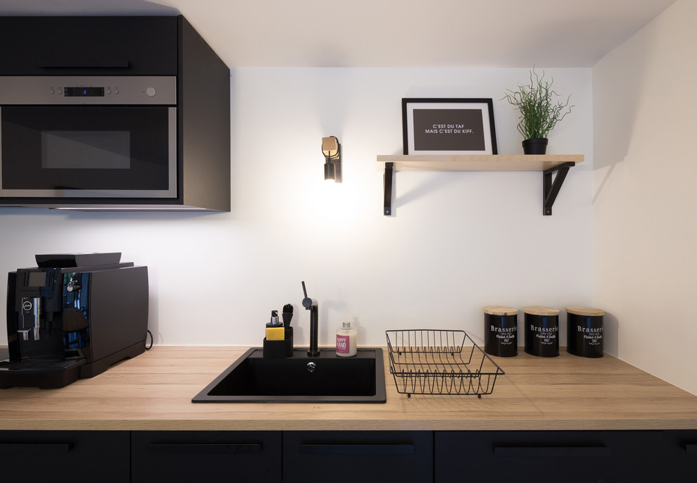 Photo of a mid-sized industrial l-shaped separate kitchen in Paris with a single-bowl sink, beaded inset cabinets, black cabinets, wood benchtops, white splashback, stainless steel appliances, linoleum floors, no island, grey floor and brown benchtop.