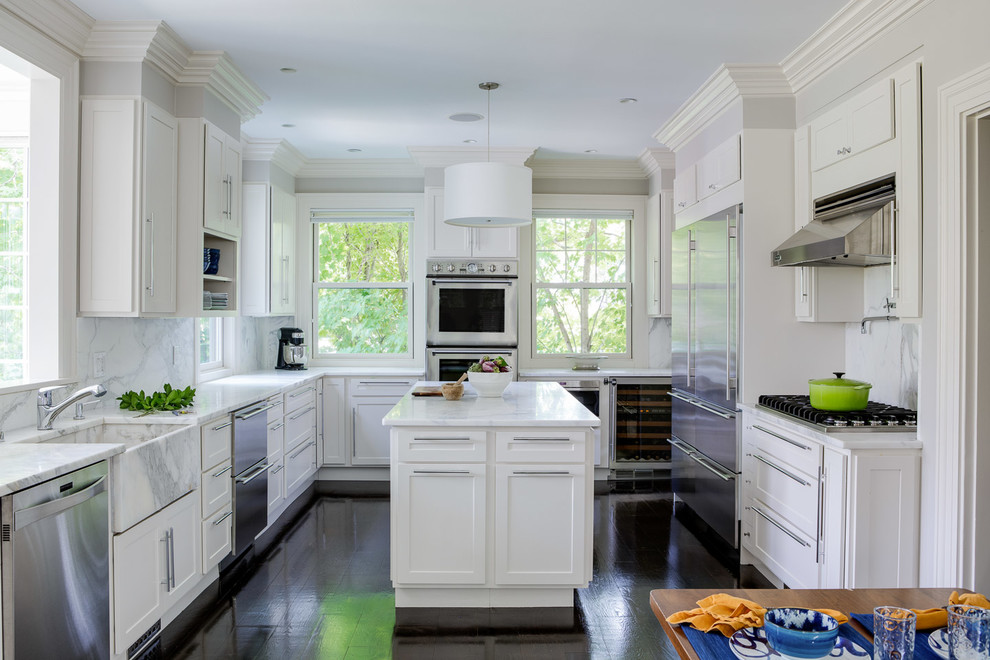Traditional kitchen in Boston with a farmhouse sink, shaker cabinets, white cabinets, white splashback, marble splashback, stainless steel appliances, dark hardwood floors, with island and white benchtop.