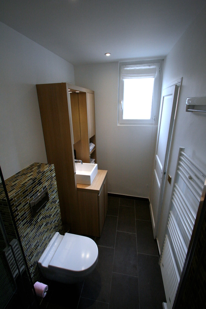 Photo of a mid-sized scandinavian 3/4 bathroom in Paris with beaded inset cabinets, light wood cabinets, a curbless shower, a wall-mount toilet, multi-coloured tile, ceramic tile, white walls, ceramic floors, a vessel sink, granite benchtops and a sliding shower screen.