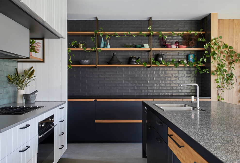 Photo of a contemporary kitchen in Sydney with a drop-in sink, flat-panel cabinets, black cabinets, grey splashback, subway tile splashback, stainless steel appliances, with island, grey floor and black benchtop.