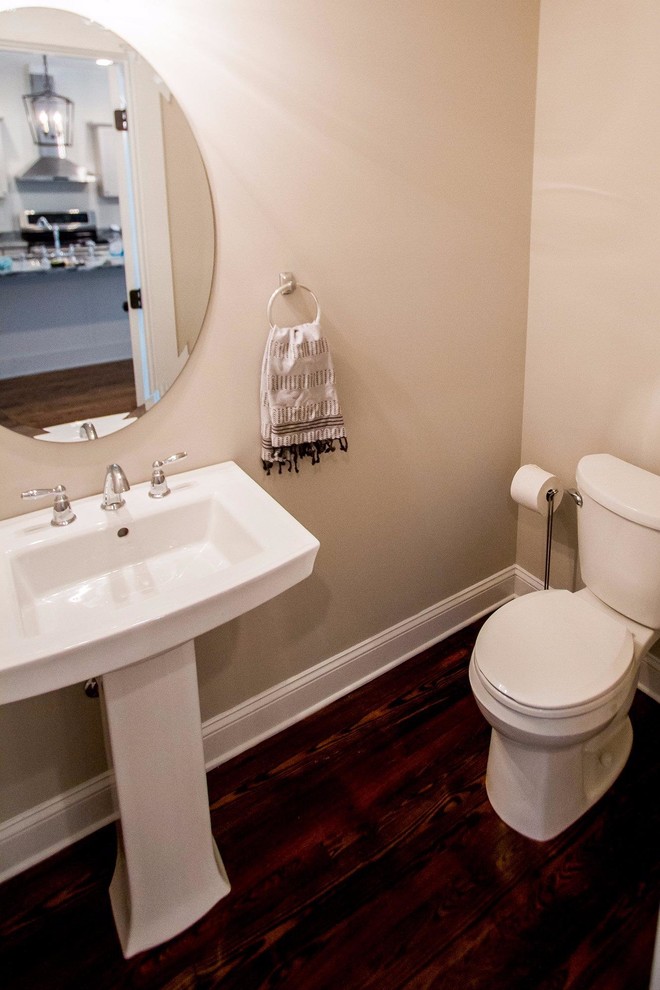 Photo of a mid-sized traditional powder room in Other with open cabinets, a two-piece toilet, beige walls, dark hardwood floors, a pedestal sink and brown floor.