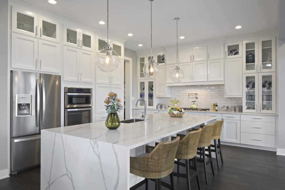 Large transitional l-shaped dark wood floor and brown floor kitchen photo in DC Metro with a farmhouse sink, recessed-panel cabinets, white cabinets, quartzite countertops, white backsplash, subway tile backsplash, stainless steel appliances, an island and white countertops