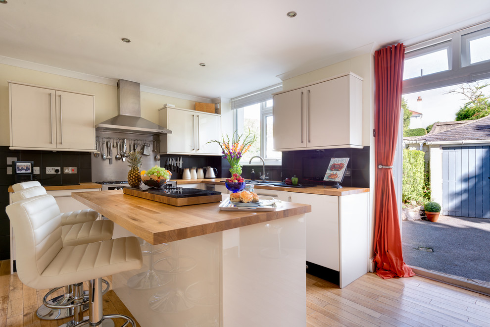 Inspiration for a mid-sized contemporary l-shaped kitchen in Devon with flat-panel cabinets, white cabinets, black splashback, stone slab splashback, stainless steel appliances, medium hardwood floors and with island.