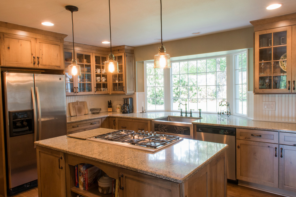 Example of a mid-sized mountain style u-shaped medium tone wood floor enclosed kitchen design with a farmhouse sink, shaker cabinets, medium tone wood cabinets, granite countertops, beige backsplash, ceramic backsplash, stainless steel appliances and an island