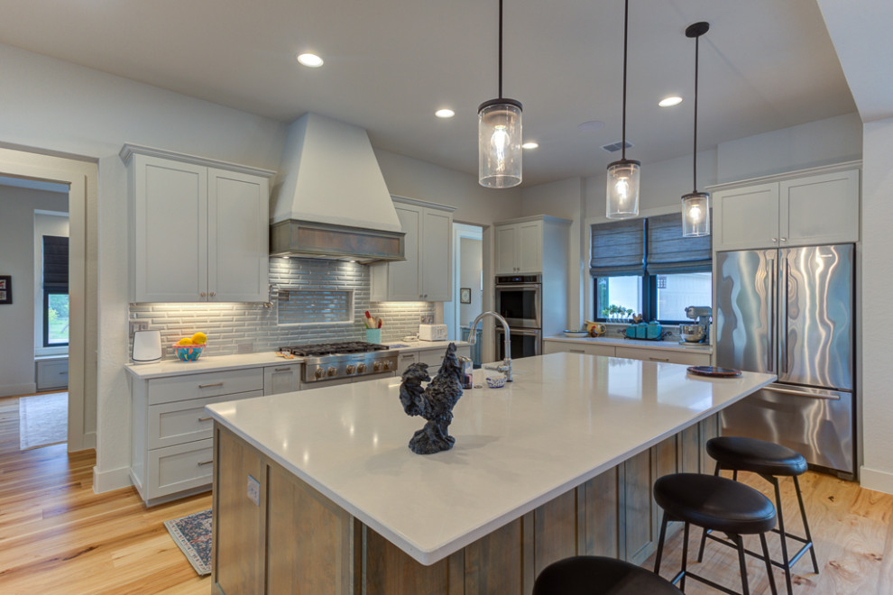 Example of a mid-sized transitional light wood floor, beige floor and vaulted ceiling kitchen design in Austin with a farmhouse sink, shaker cabinets, gray cabinets, quartz countertops, gray backsplash, glass tile backsplash, stainless steel appliances, an island and gray countertops