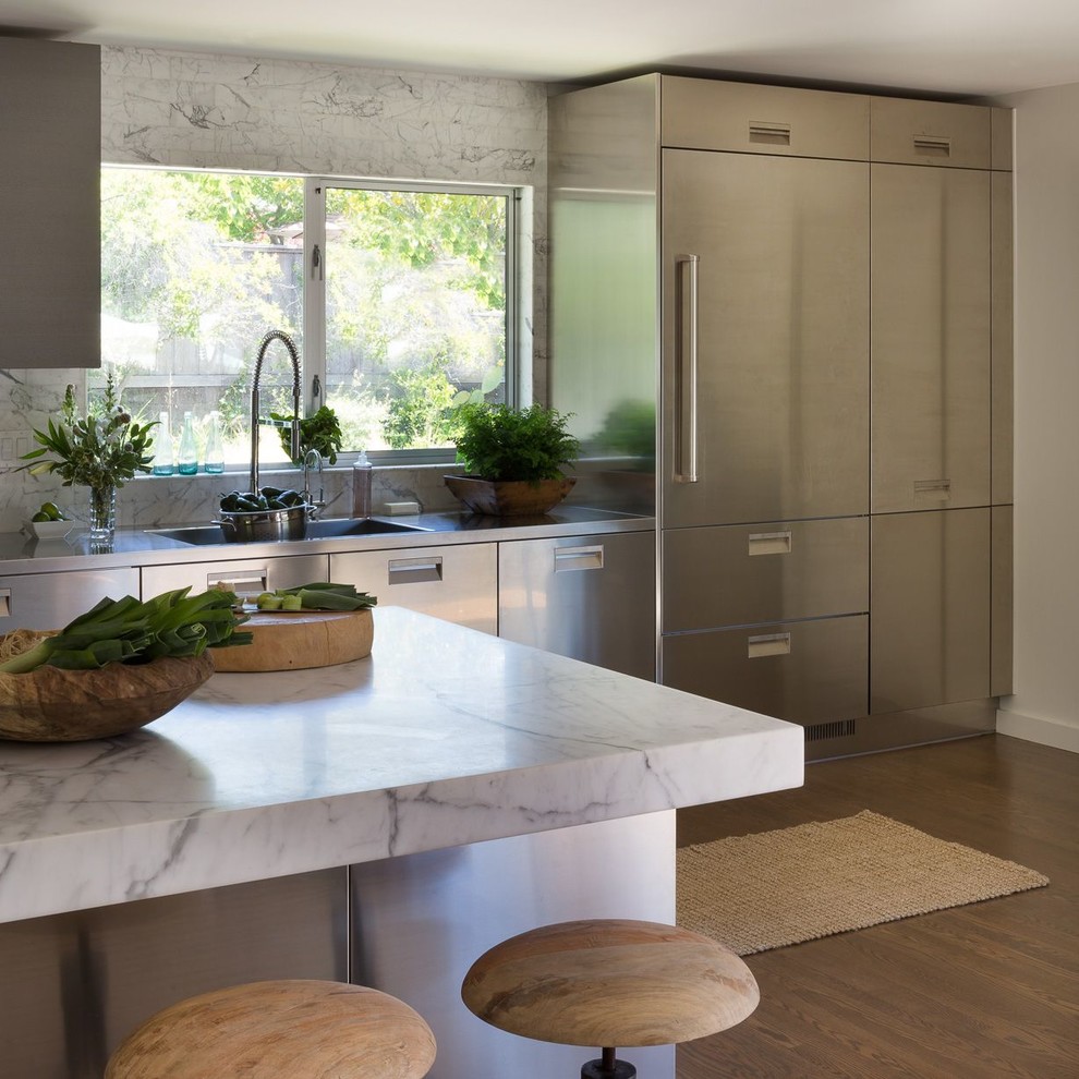 Mid-sized modern single-wall eat-in kitchen in San Francisco with an integrated sink, flat-panel cabinets, stainless steel cabinets, marble benchtops, white splashback, marble splashback, stainless steel appliances, medium hardwood floors, with island and white benchtop.