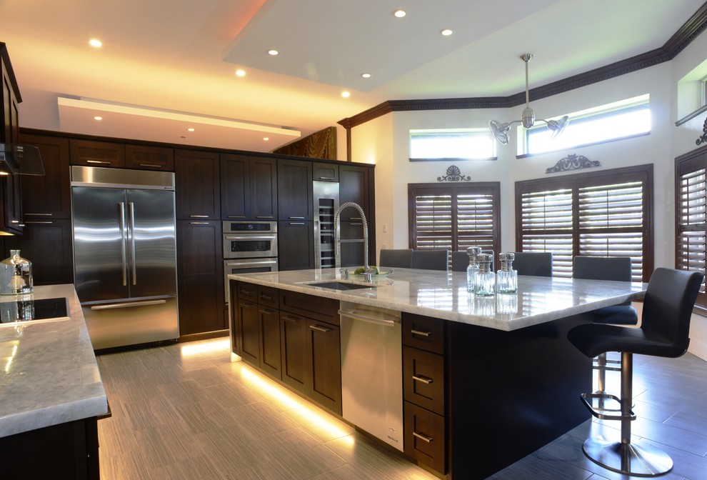 This is an example of a large transitional l-shaped eat-in kitchen in Miami with an undermount sink, shaker cabinets, dark wood cabinets, marble benchtops, grey splashback, glass tile splashback, stainless steel appliances, light hardwood floors and with island.