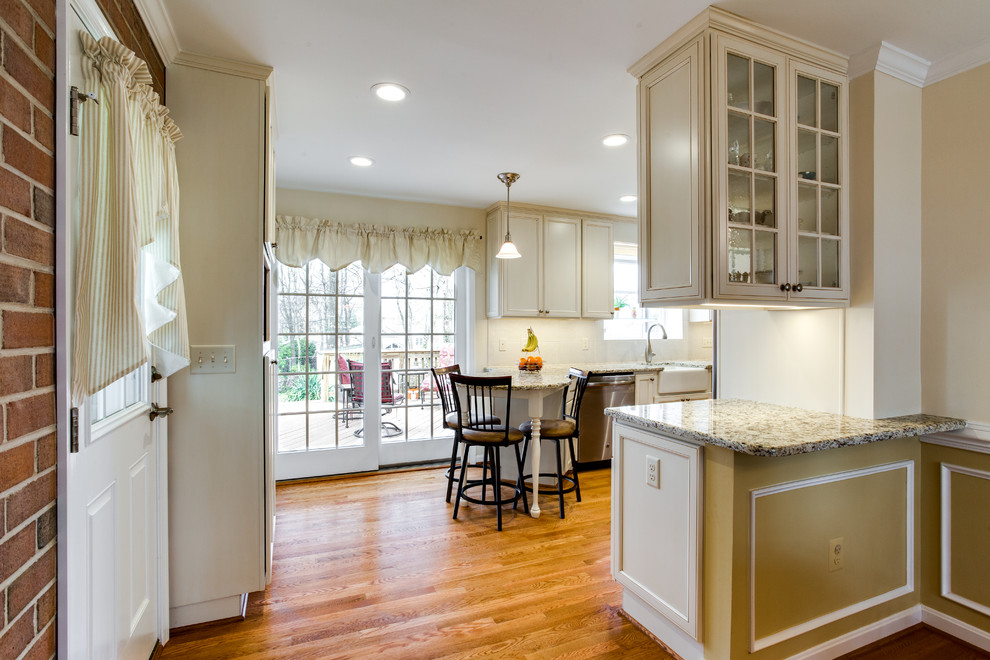 Photo of a mid-sized country galley eat-in kitchen in DC Metro with a farmhouse sink, recessed-panel cabinets, white cabinets, quartzite benchtops, beige splashback, ceramic splashback, stainless steel appliances, medium hardwood floors, a peninsula and brown floor.