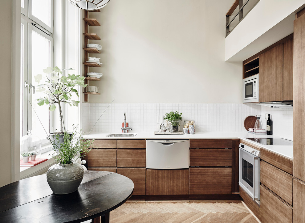 Photo of a mid-sized scandinavian l-shaped eat-in kitchen in Gothenburg with a drop-in sink, flat-panel cabinets, medium wood cabinets, white splashback, stainless steel appliances, light hardwood floors and no island.