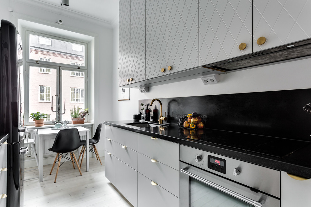 Photo of a mid-sized scandinavian single-wall kitchen in Stockholm with beaded inset cabinets, grey cabinets, granite benchtops, no island, a single-bowl sink, stone slab splashback, stainless steel appliances and light hardwood floors.