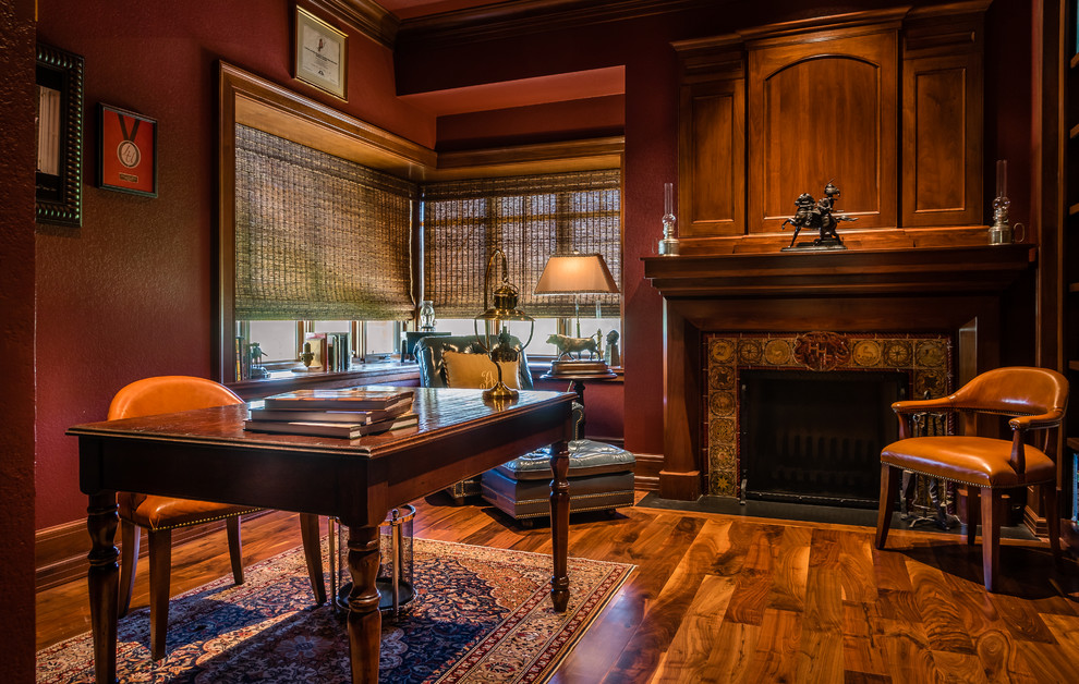 Large country study room in Houston with red walls, medium hardwood floors, a two-sided fireplace, a wood fireplace surround, a freestanding desk and brown floor.