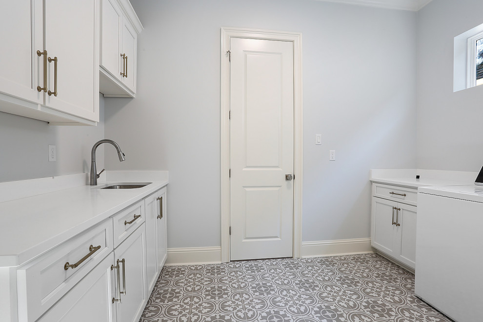 Photo of a mid-sized traditional galley dedicated laundry room in New Orleans with an undermount sink, shaker cabinets, white cabinets, quartzite benchtops, white splashback, engineered quartz splashback, grey walls, porcelain floors, a side-by-side washer and dryer, grey floor and white benchtop.