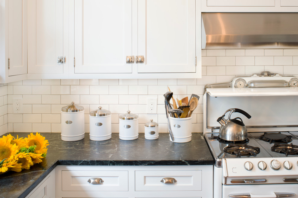Inspiration for a mid-sized arts and crafts kitchen in San Francisco with shaker cabinets, white cabinets, white splashback, porcelain splashback, medium hardwood floors, with island, a farmhouse sink and black benchtop.