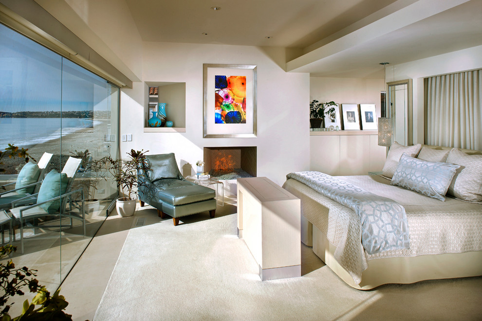 Photo of a large beach style bedroom in Orange County with beige walls, a standard fireplace, carpet and a plaster fireplace surround.