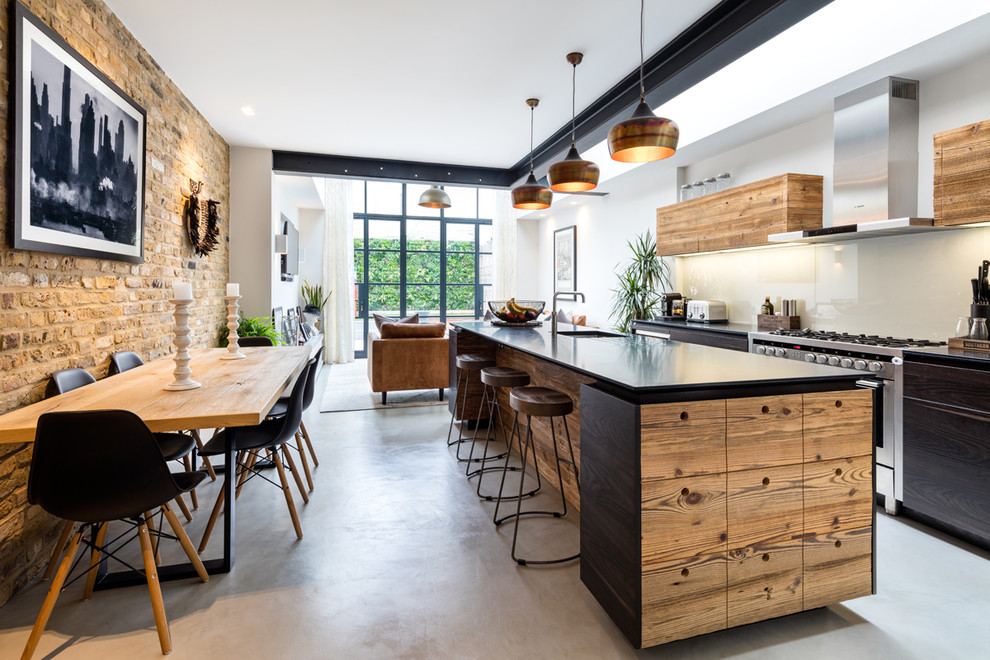 Inspiration for a mid-sized industrial eat-in kitchen in West Midlands with an undermount sink, flat-panel cabinets, dark wood cabinets, glass sheet splashback, stainless steel appliances, concrete floors, with island and grey floor.