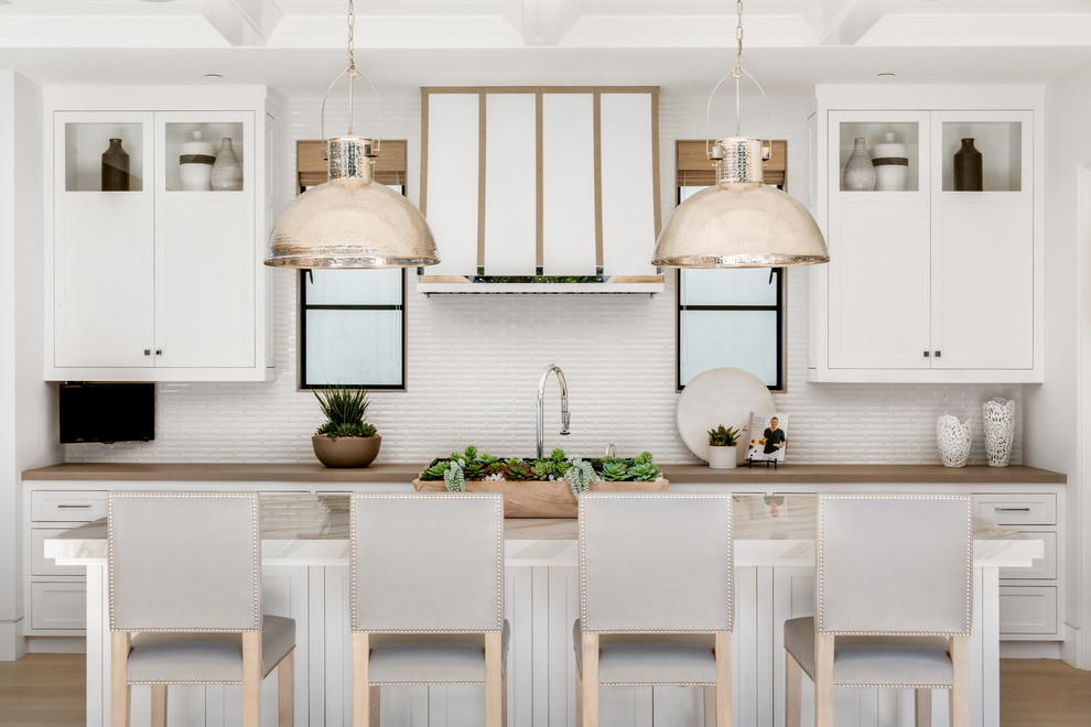 Beach style kitchen in Orange County with shaker cabinets, white cabinets, white splashback, light hardwood floors, with island, beige floor and brown benchtop.
