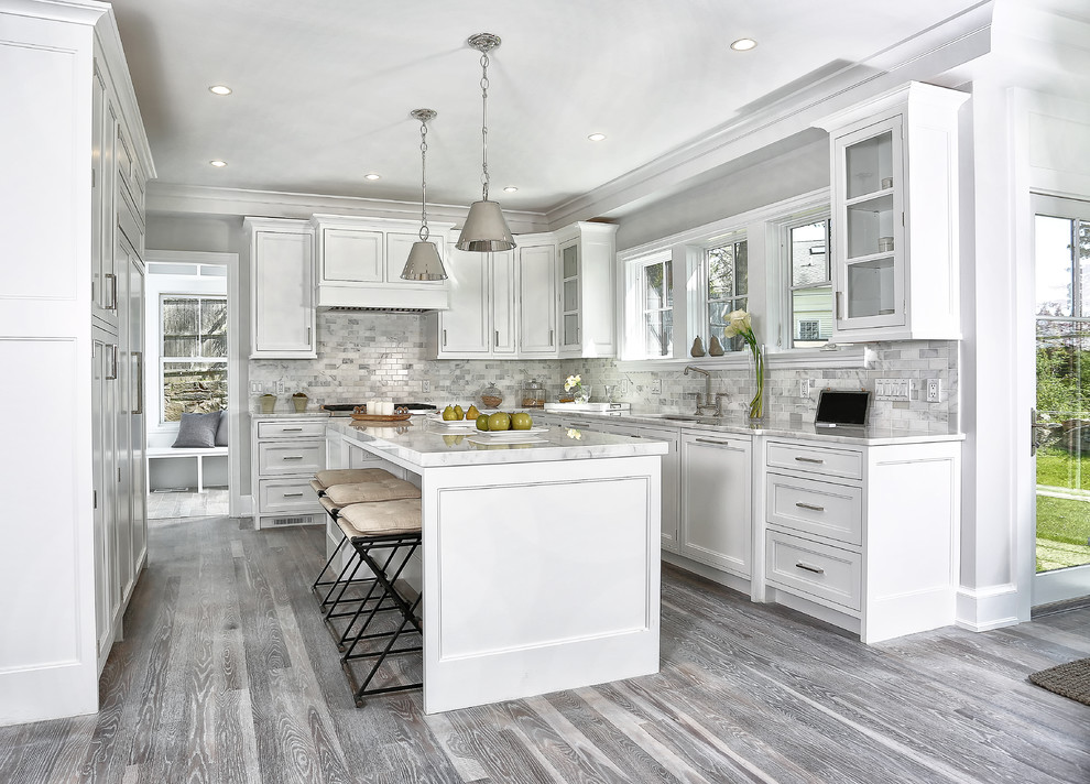This is an example of a mid-sized beach style u-shaped eat-in kitchen in New York with an undermount sink, recessed-panel cabinets, white cabinets, multi-coloured splashback, panelled appliances, light hardwood floors, with island, marble benchtops, marble splashback and grey floor.