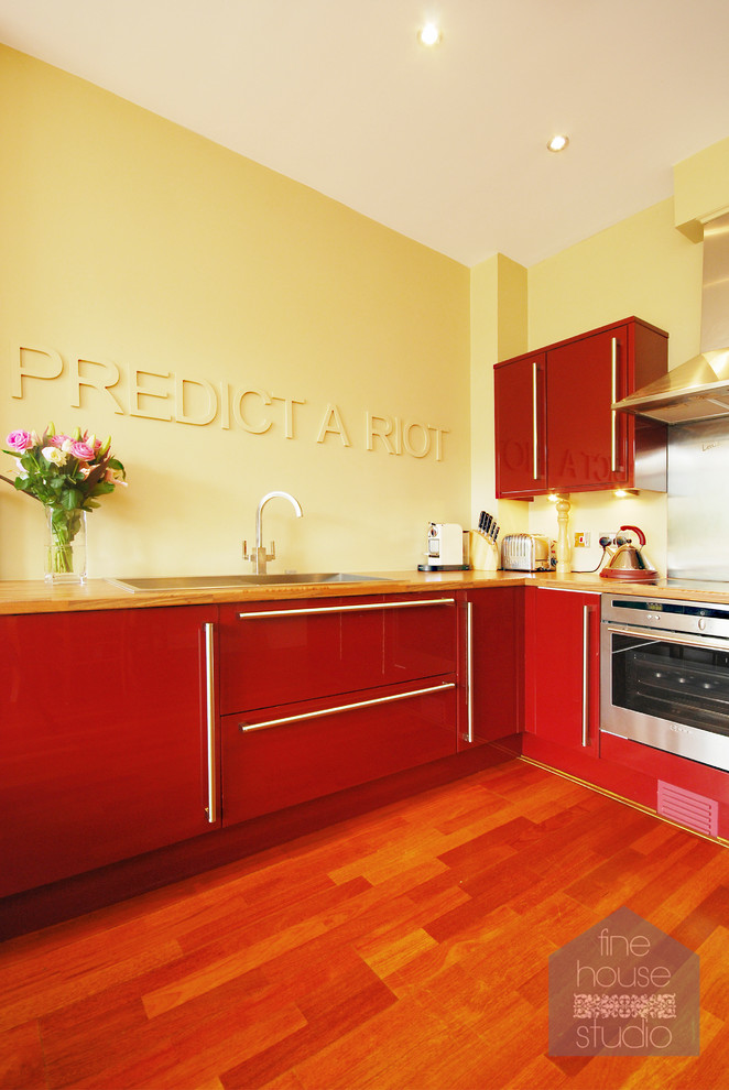 This is an example of a large modern l-shaped eat-in kitchen in Gloucestershire with an integrated sink, shaker cabinets, red cabinets, wood benchtops, metallic splashback, stainless steel appliances and dark hardwood floors.