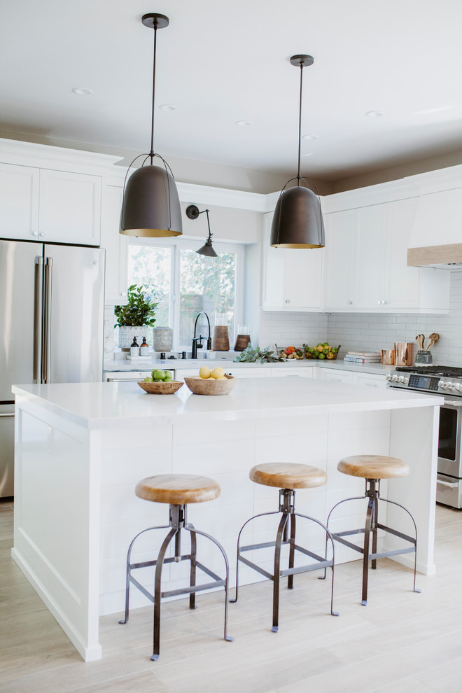 Photo of a mid-sized beach style l-shaped open plan kitchen in San Diego with an undermount sink, shaker cabinets, white cabinets, quartz benchtops, white splashback, subway tile splashback, stainless steel appliances, ceramic floors, with island and brown floor.