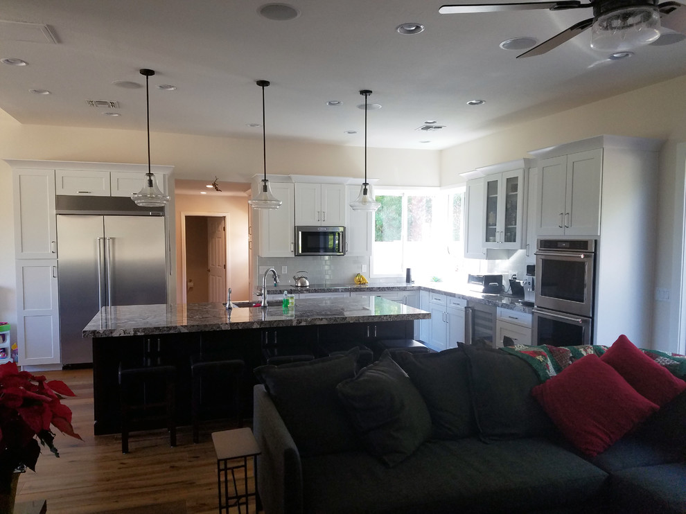Eat-in kitchen - large transitional l-shaped medium tone wood floor eat-in kitchen idea in Phoenix with an undermount sink, shaker cabinets, white cabinets, granite countertops, gray backsplash, subway tile backsplash, stainless steel appliances and an island