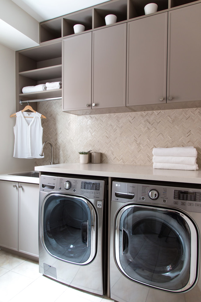 Mid-sized contemporary single-wall utility room in Toronto with a side-by-side washer and dryer, beige floor, a drop-in sink, shaker cabinets, beige cabinets, quartz benchtops, beige walls, ceramic floors and beige benchtop.