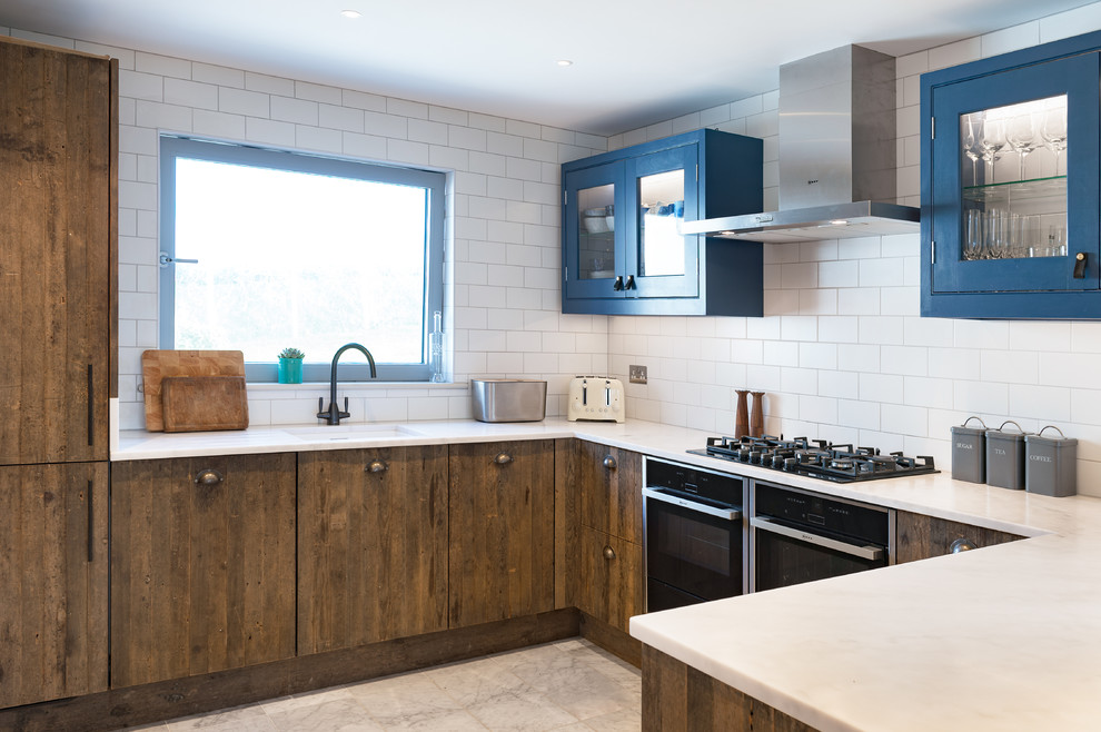Photo of a mid-sized country u-shaped open plan kitchen in Cornwall with white splashback, ceramic splashback, black appliances, a peninsula, white benchtop, an undermount sink, flat-panel cabinets, dark wood cabinets and grey floor.