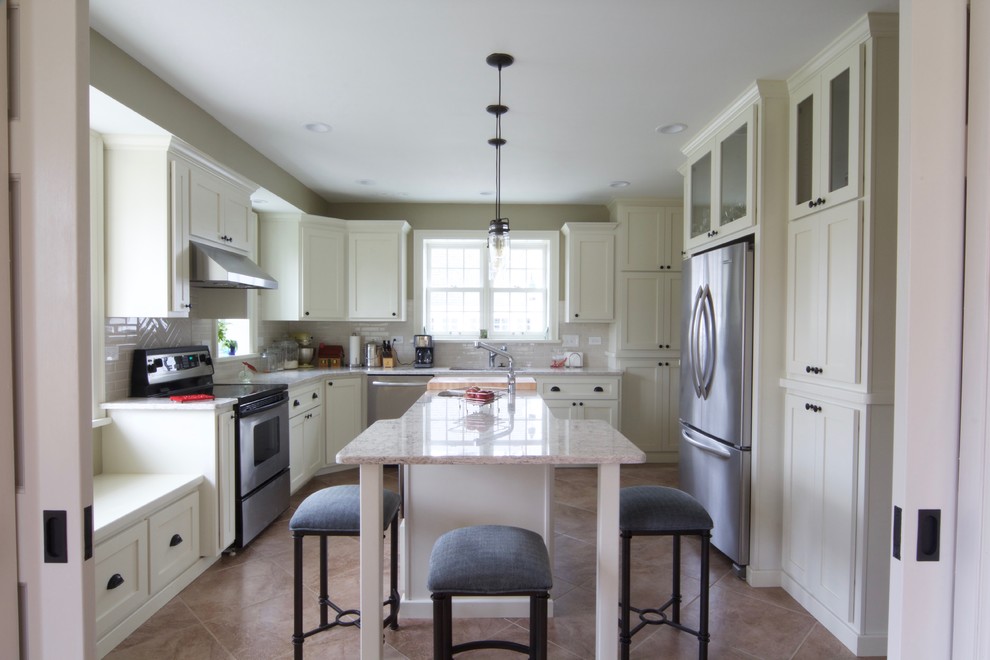 Mid-sized traditional u-shaped kitchen pantry in Chicago with an undermount sink, flat-panel cabinets, beige cabinets, white splashback, subway tile splashback, stainless steel appliances, ceramic floors, with island, granite benchtops and brown floor.