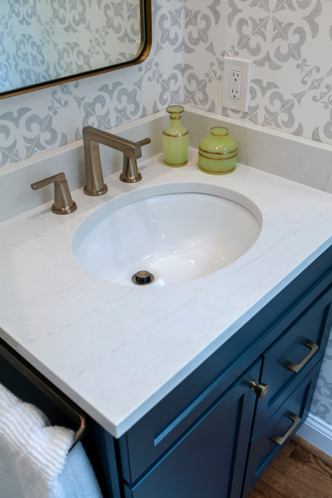 This is an example of a small transitional powder room in Philadelphia with shaker cabinets, blue cabinets, grey walls, medium hardwood floors, a console sink, quartzite benchtops, brown floor and white benchtops.