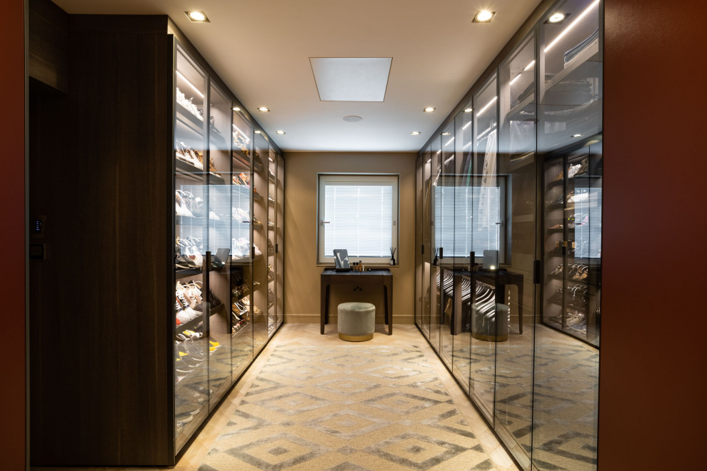 Expansive contemporary gender-neutral walk-in wardrobe in London with glass-front cabinets, dark wood cabinets, light hardwood floors and beige floor.