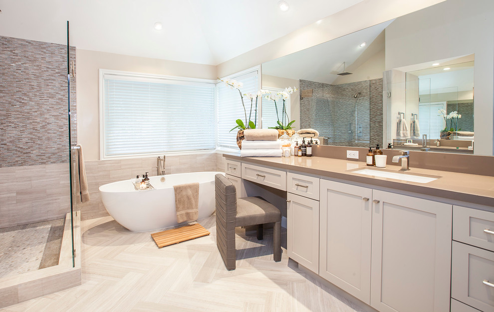 Beach style master bathroom in Orange County with an undermount sink, shaker cabinets, grey cabinets, engineered quartz benchtops, a freestanding tub, a corner shower, a one-piece toilet, gray tile, stone tile, grey walls and limestone floors.