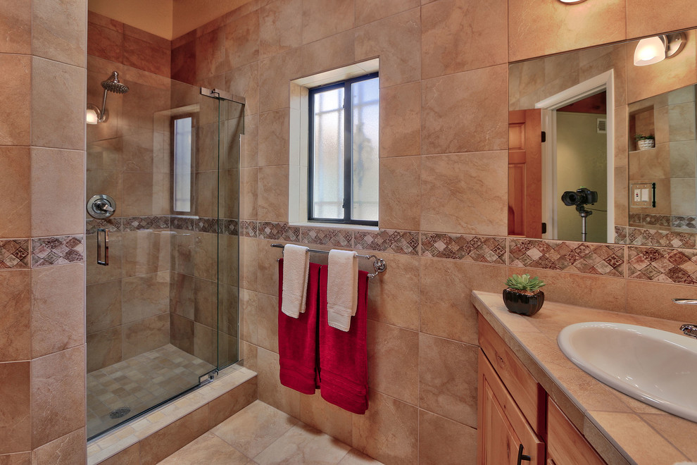 Inspiration for an expansive 3/4 bathroom in Albuquerque with shaker cabinets, medium wood cabinets, a corner shower, a two-piece toilet, beige tile, ceramic tile, beige walls, ceramic floors, a drop-in sink and tile benchtops.