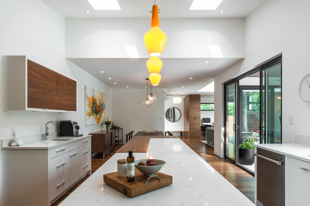 Mid-sized midcentury u-shaped open plan kitchen in Vancouver with an undermount sink, flat-panel cabinets, white cabinets, quartz benchtops, grey splashback, ceramic splashback, stainless steel appliances, medium hardwood floors, with island and brown floor.