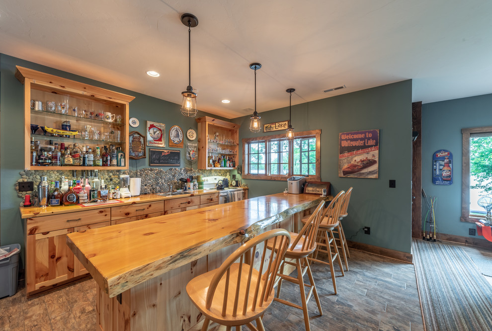 Inspiration for a mid-sized country galley seated home bar in Milwaukee with a drop-in sink, recessed-panel cabinets, yellow cabinets, wood benchtops, multi-coloured splashback, stone tile splashback, ceramic floors, brown floor and yellow benchtop.