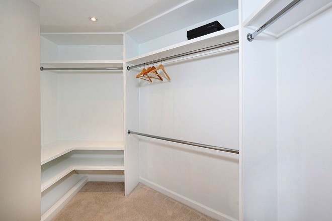 This is an example of a mid-sized beach style gender-neutral walk-in wardrobe in Orange County with flat-panel cabinets, white cabinets, carpet and beige floor.