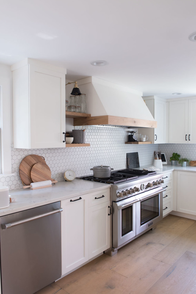 This is an example of a large country u-shaped eat-in kitchen in Boston with shaker cabinets, white cabinets, quartz benchtops, white splashback, mosaic tile splashback, stainless steel appliances, light hardwood floors, a peninsula, brown floor and white benchtop.