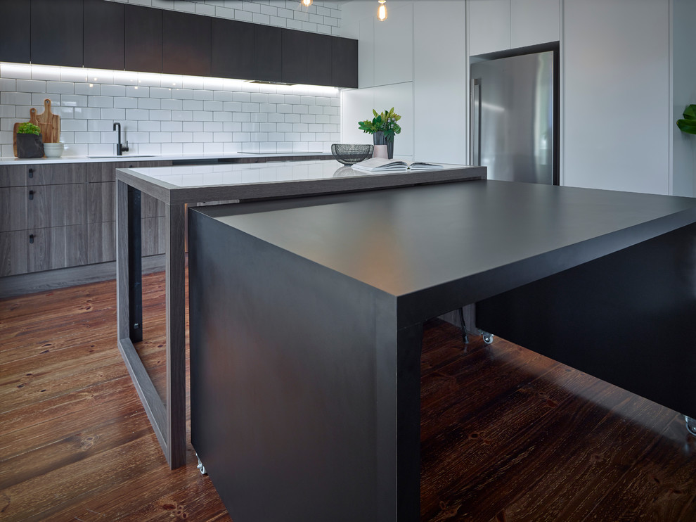 Photo of a large contemporary single-wall eat-in kitchen in Other with an undermount sink, white splashback, ceramic splashback, stainless steel appliances, medium hardwood floors, with island, flat-panel cabinets, dark wood cabinets, solid surface benchtops and white benchtop.