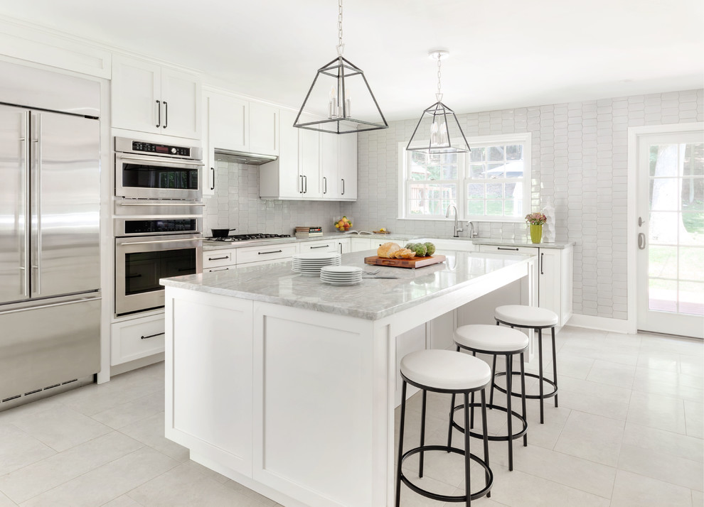 Photo of a beach style l-shaped kitchen in New York with a farmhouse sink, shaker cabinets, white cabinets, marble benchtops, grey splashback, stainless steel appliances, with island, grey floor and grey benchtop.