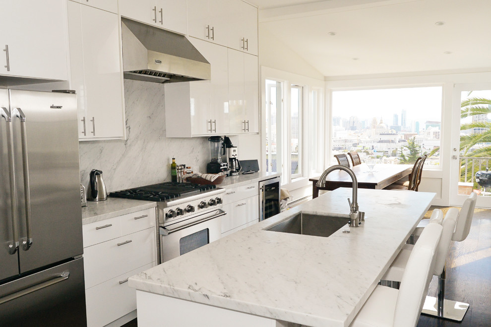 Contemporary galley eat-in kitchen in San Francisco with an undermount sink, flat-panel cabinets, white cabinets, white splashback, stainless steel appliances, dark hardwood floors, with island and marble benchtops.