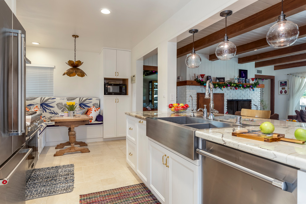Mid-sized transitional l-shaped eat-in kitchen in Los Angeles with a farmhouse sink, white cabinets, granite benchtops, stainless steel appliances, no island, white splashback, ceramic splashback, travertine floors and recessed-panel cabinets.