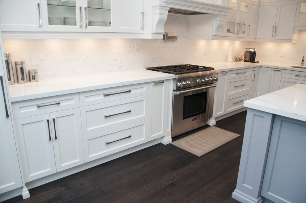 Large transitional l-shaped dark wood floor and brown floor enclosed kitchen photo in Toronto with an undermount sink, shaker cabinets, white cabinets, quartz countertops, white backsplash, marble backsplash, stainless steel appliances, an island and white countertops
