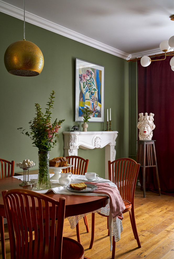 Cette image montre une salle à manger bohème fermée et de taille moyenne avec un mur vert, un sol en bois brun, une cheminée standard, un manteau de cheminée en plâtre, un sol marron, poutres apparentes et du papier peint.
