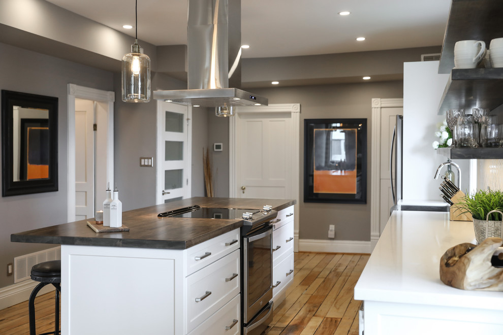 Eat-in kitchen - mid-sized transitional single-wall medium tone wood floor and brown floor eat-in kitchen idea with a farmhouse sink, shaker cabinets, white cabinets, white backsplash, stainless steel appliances, an island and white countertops